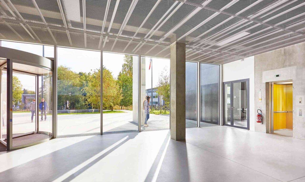 Interior of a modern building with glass panels, a yellow elevator, and smooth floors.