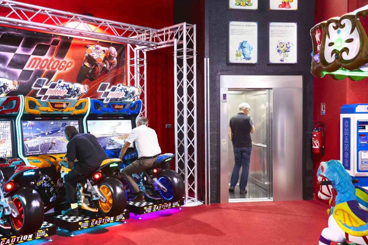 Arcade area with motorcycle racing machines, an elevator, and colorful decorations.